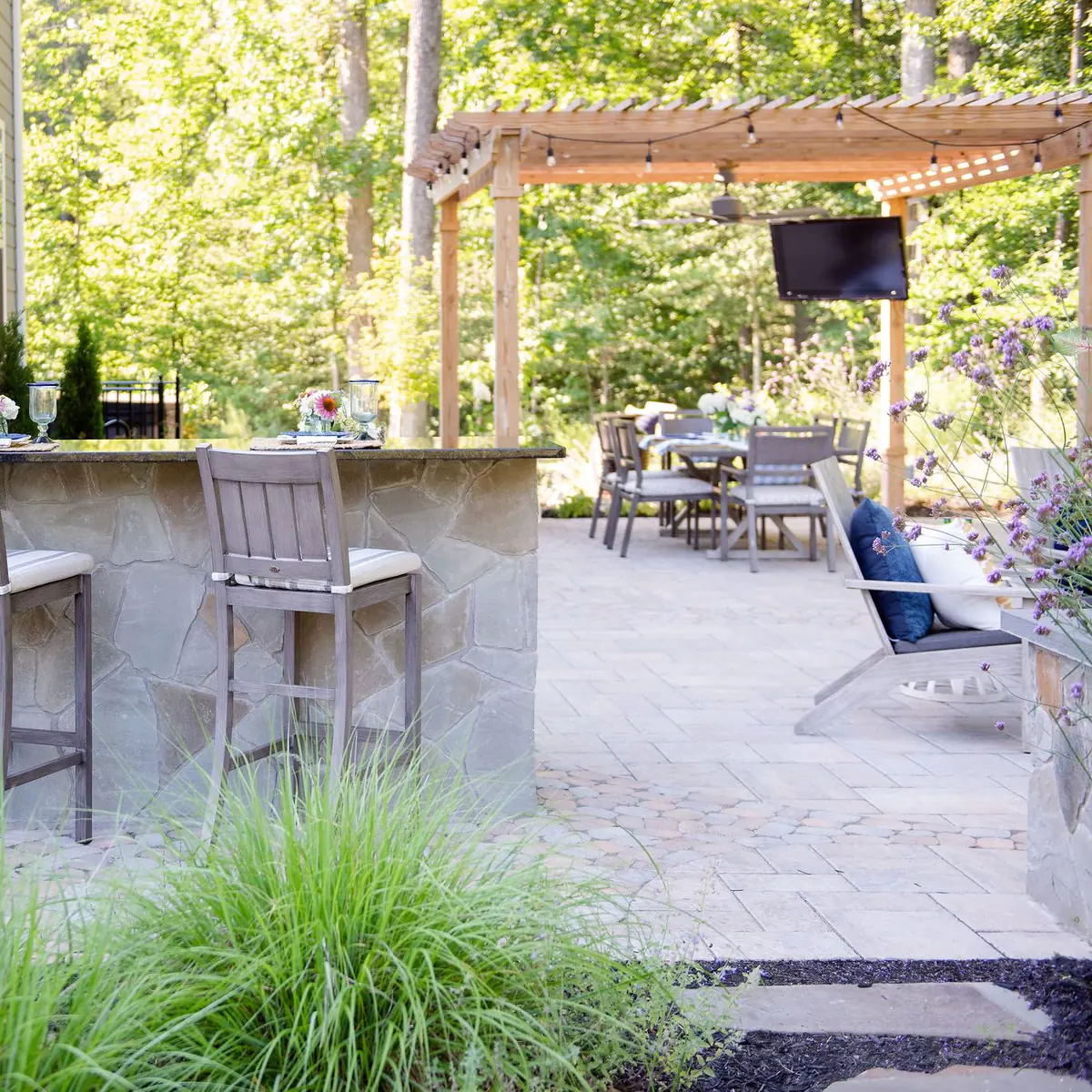 Expansive patio with pergola, outdoor television, bar top seating, outdoor kitchen, fire pit, and landscaping.
