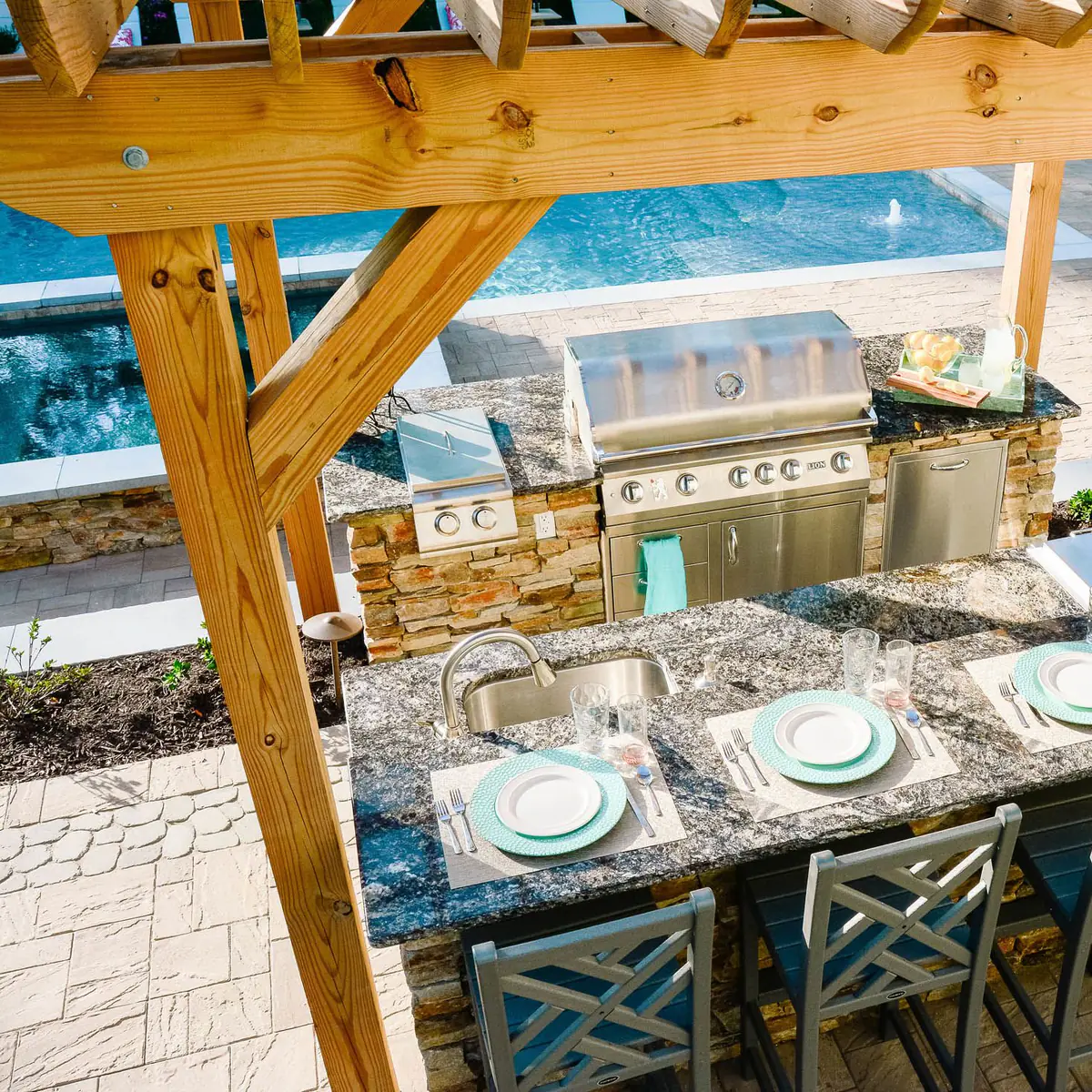 outdoor kitchen with granite countertops and grill island under a pergola