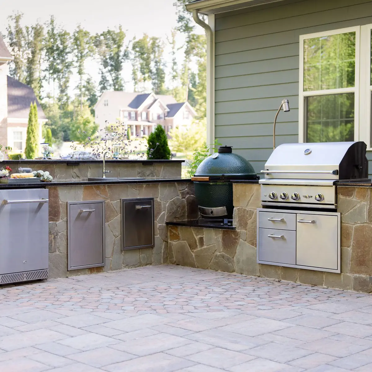 Outdoor kitchen with grill, egg smoker, refrigerator, and bar top seating
