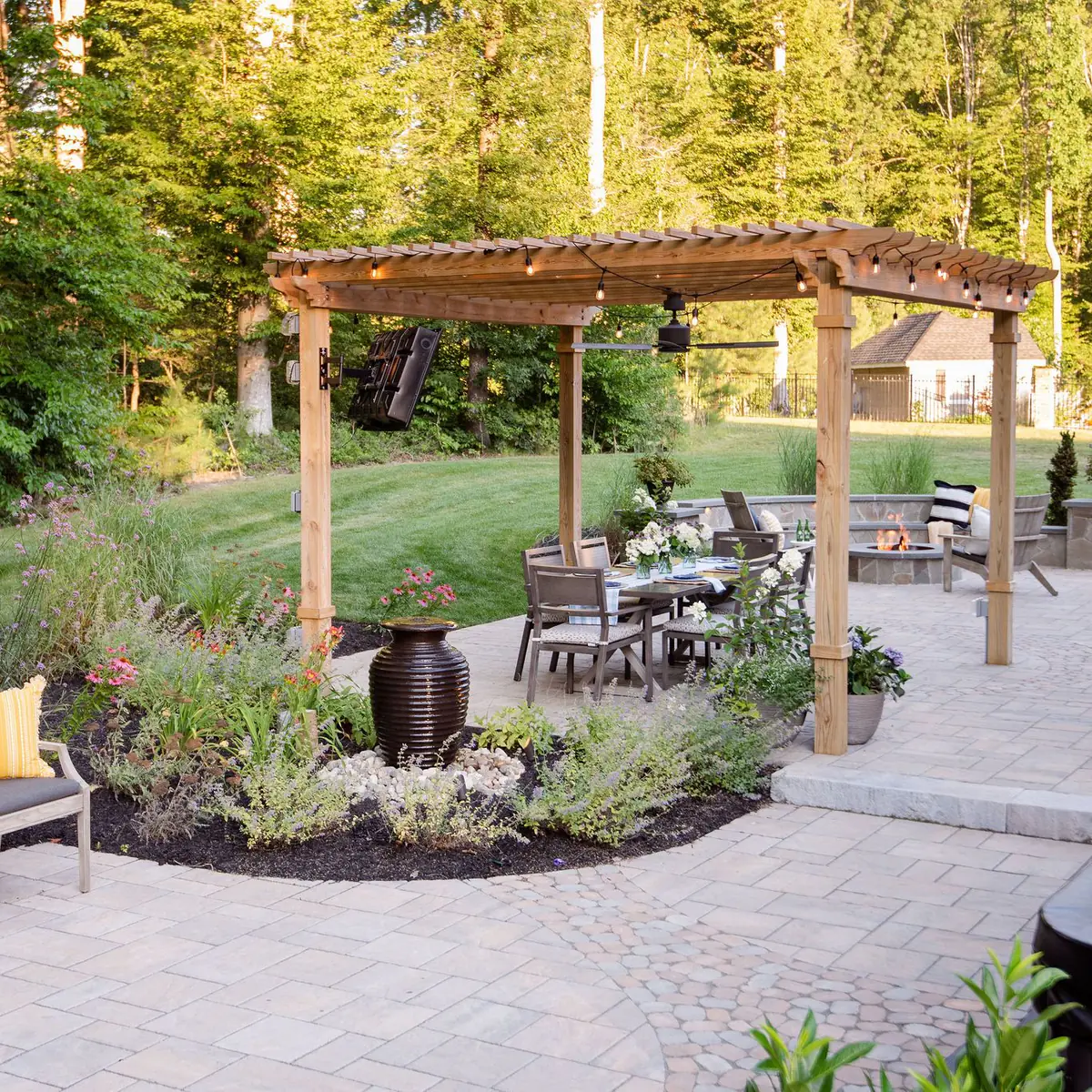 Expansive paver patio with landscaping, bubbling urn, pergola, hot tub, and fire pit.